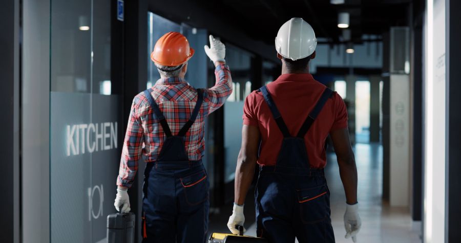 Caucasian engineer and african electric technician walking inside building hallway and inspecting light bulbs, controling electric system and coworking.