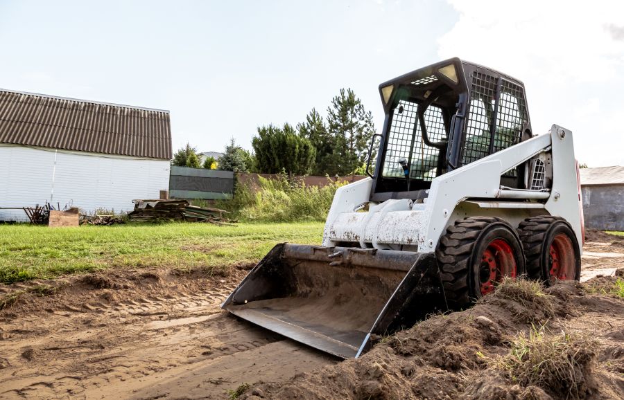 A skid steer loader clears the site for construction. Land work by the territory improvement. Machine for work in confined areas. Small tractor with a bucket for moving soil, turf and bulk materials.