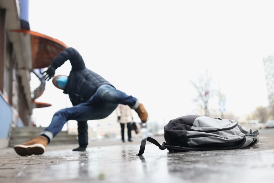 Low angle of male person get injury after falling on slippery ground in winter. Personal bag lay on asphalt ice. Accident, trauma, fracture, clumsy concept