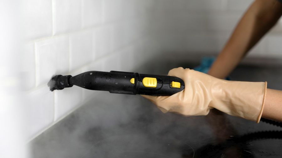 A girl cleans tiles using a steam generator. Concept of bathroom or kitchen cleaning, cleanliness. A woman