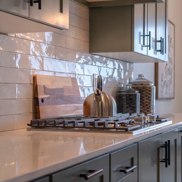 Photo Square frame Kitchen work area with cabinets cooktop countertop and tile backsplash. Dining room in front of a large window can be seen in the background.