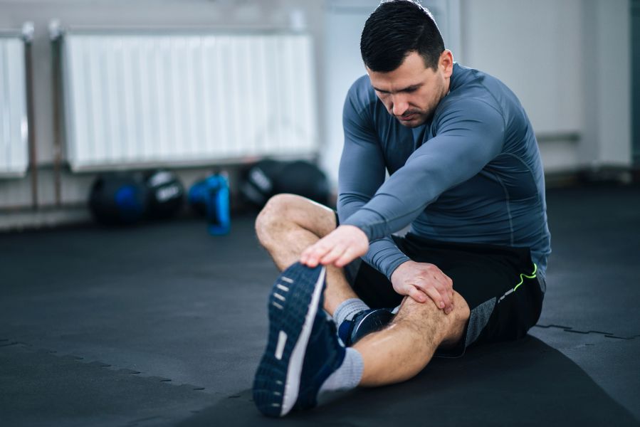 Muscular man stretching his legs before workout.